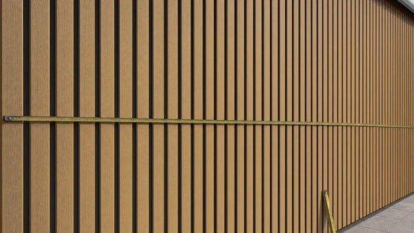 Stalen rolbandmaat gespannen over een teak composiet gevelwand om de breedte voor de gevelberekening op te meten