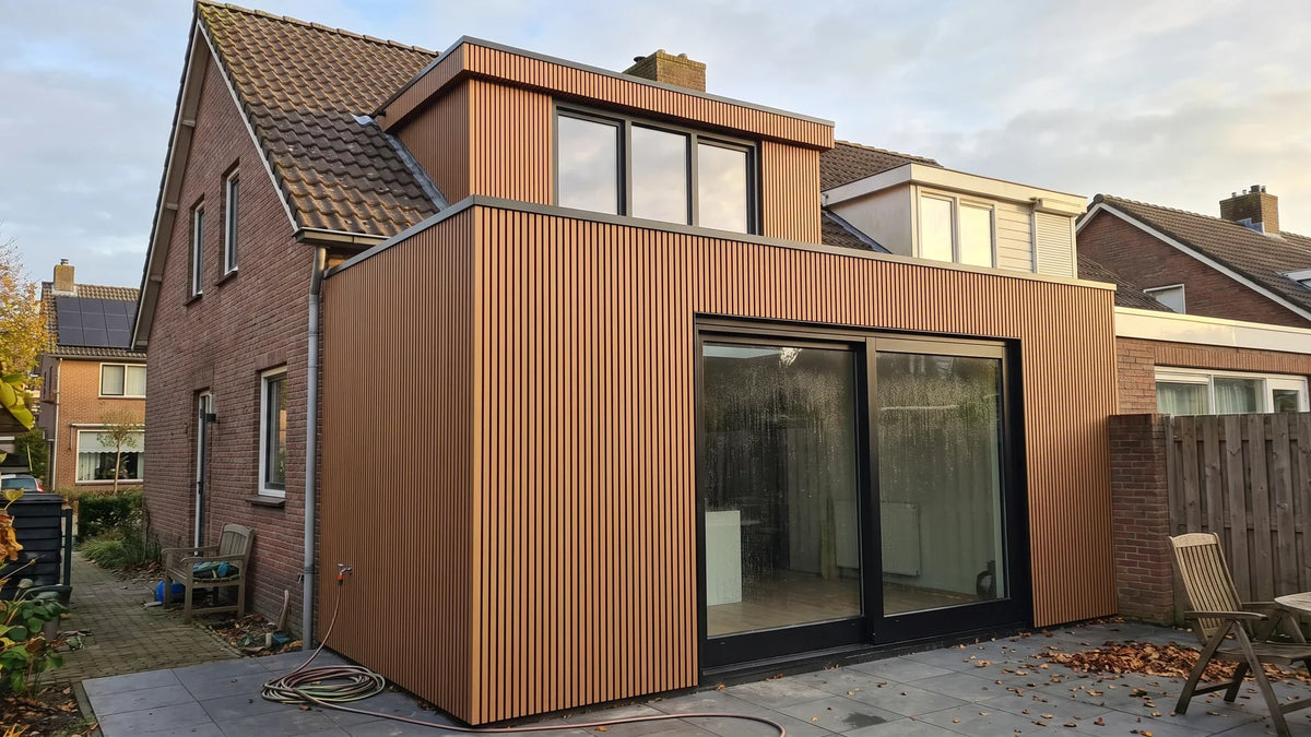 Aanbouw en dakkapel van een bestaande woning bekleed met teak composiet gevelbekleding naast roodbruin metselwerk