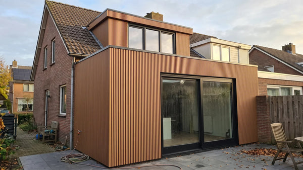 Aanbouw en dakkapel van een bestaande woning bekleed met teak composiet gevelbekleding naast roodbruin metselwerk