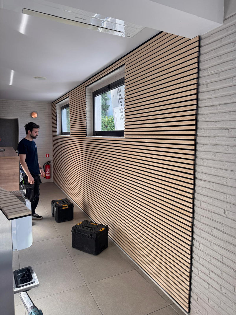Monteur bij een wand met horizontaal geplaatste akoestische wandpanelen rond twee ramen