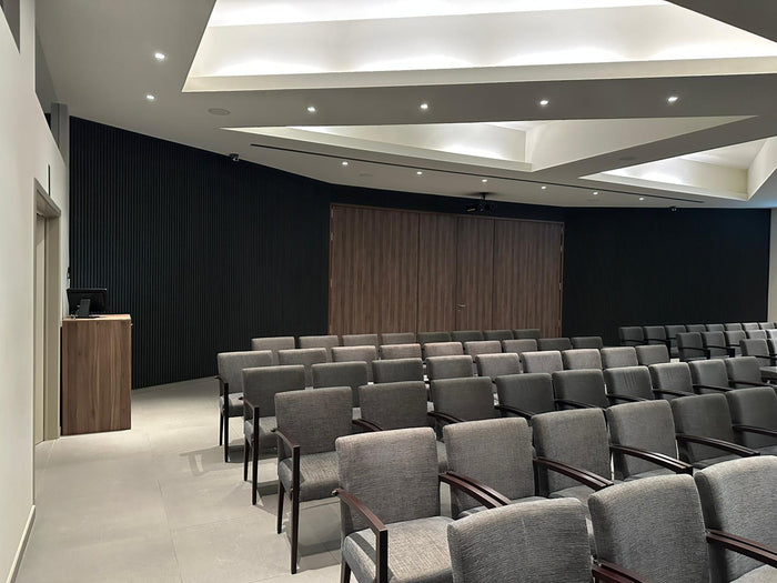 Auditorium met een wand van akoestische wandpanelen in Zwart Eiken achter rijen stoelen