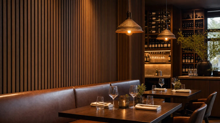 Sfeervol restauranthoekje met gerookt eiken akoestische wandpanelen, warme hanglampen en leren bankzitting