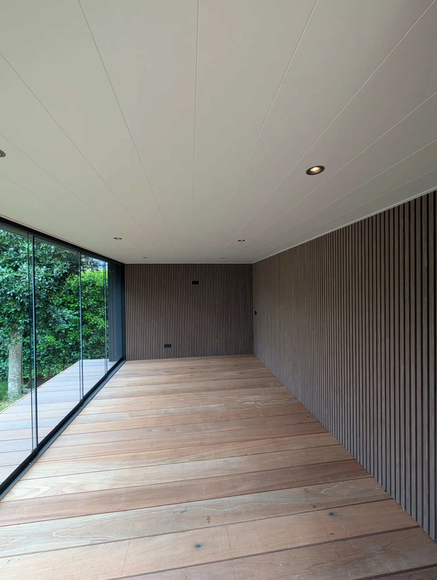 Interieur van de tuinkamer met wanden in verticale houten lattenpanelen en hardhouten vloer