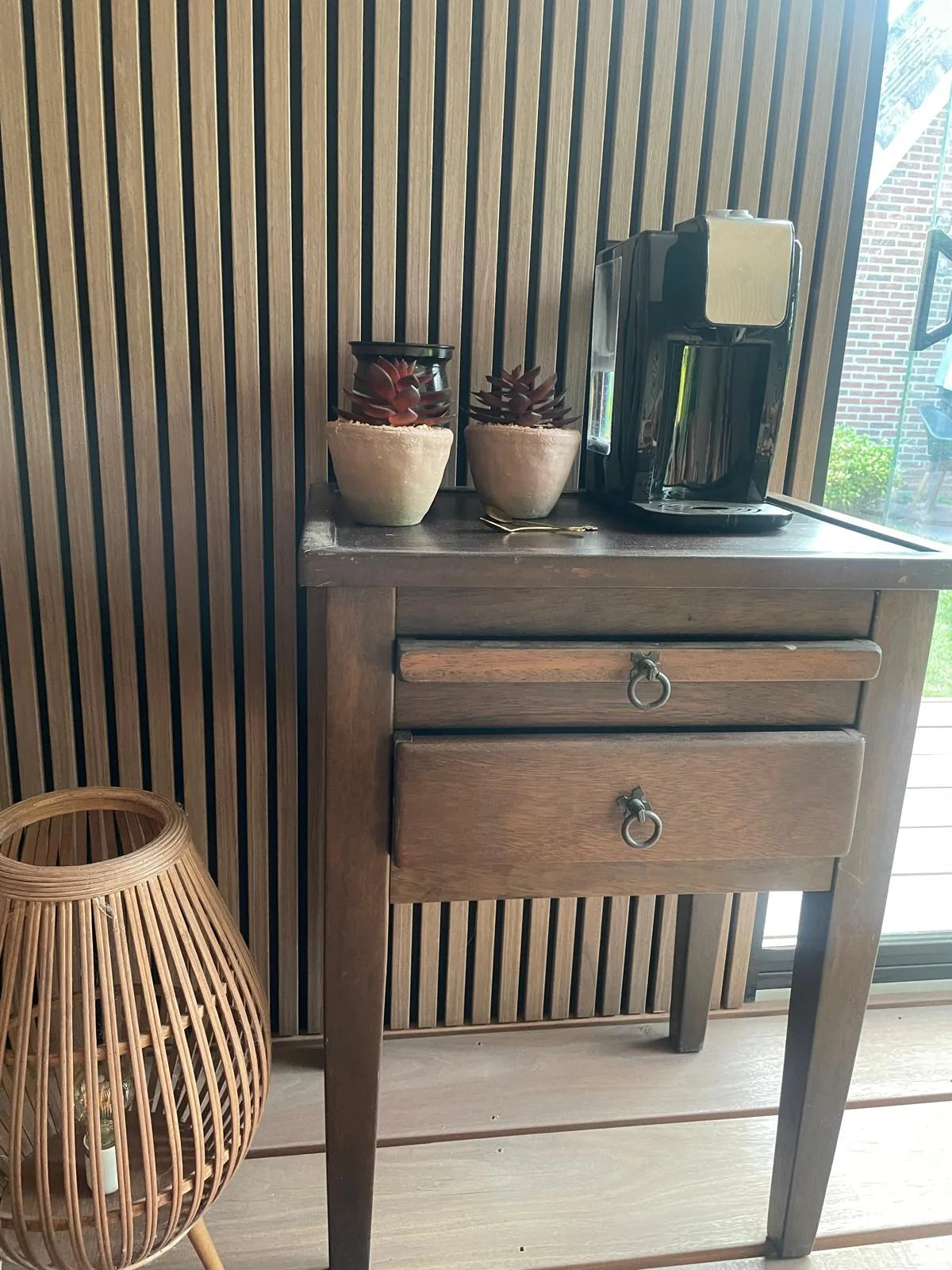 Detail van een houten lattenwand achter een antiek bijzettafeltje op een overdekte veranda