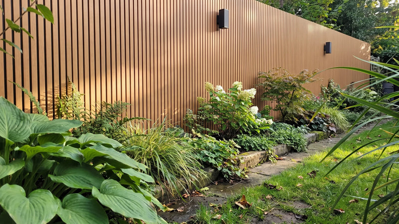 Tuinmuur bekleed met composiet gevelbekleding in Teak/Zwart, met een beplante border ervoor